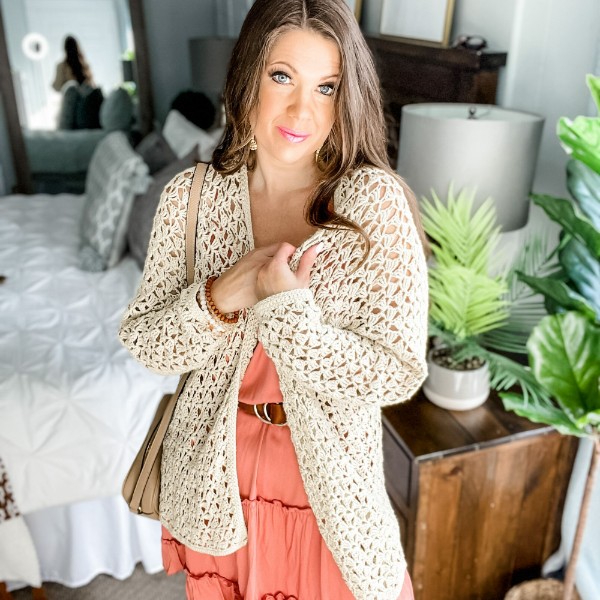 A woman wearing a lacy crochet cardigan over a summer dress.