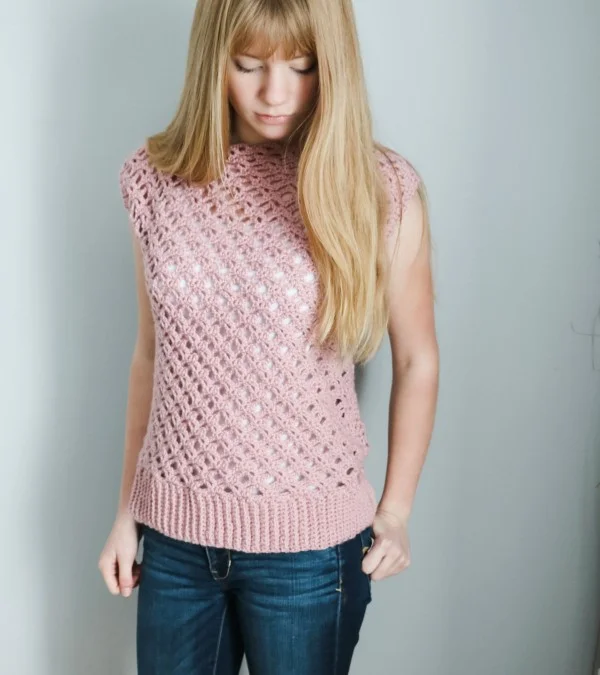 A woman wearing a short sleeved pink lace crochet top and jeans.