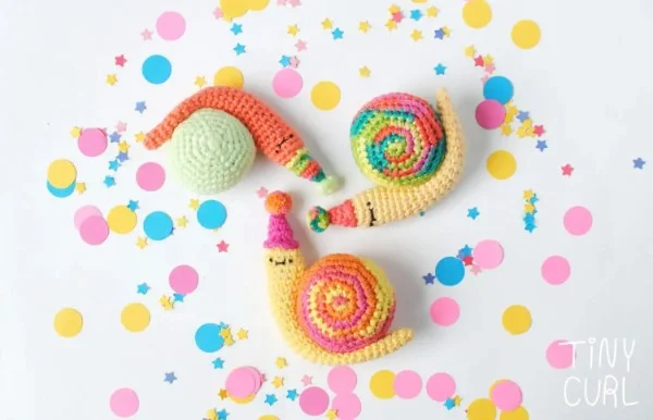 Three cute crochet snails with confetti background.