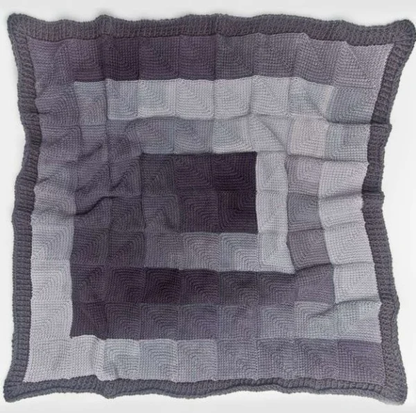 A grey Tunisian crochet blanket made from mitred squares.