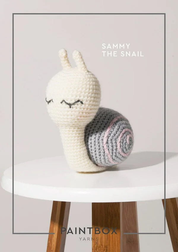 A cute crochet snail on a timber stool.