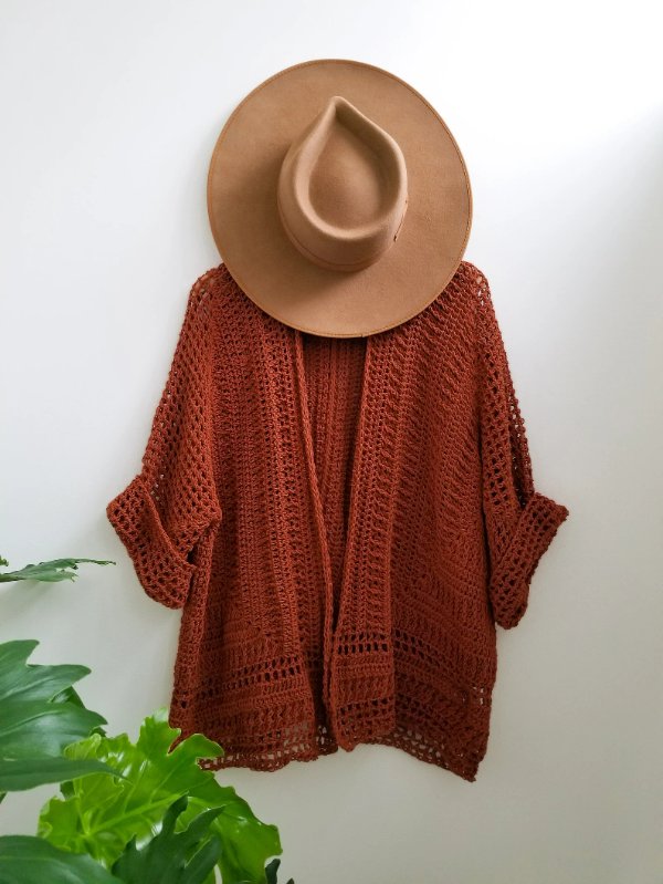A red coloured lacy crochet cardigan on a hanger with a hat.