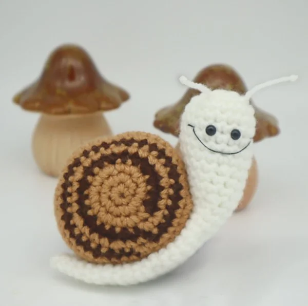 Crochet snail with mushrooms in background.
