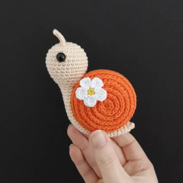 A crochet snail with a crochet flower decoration.