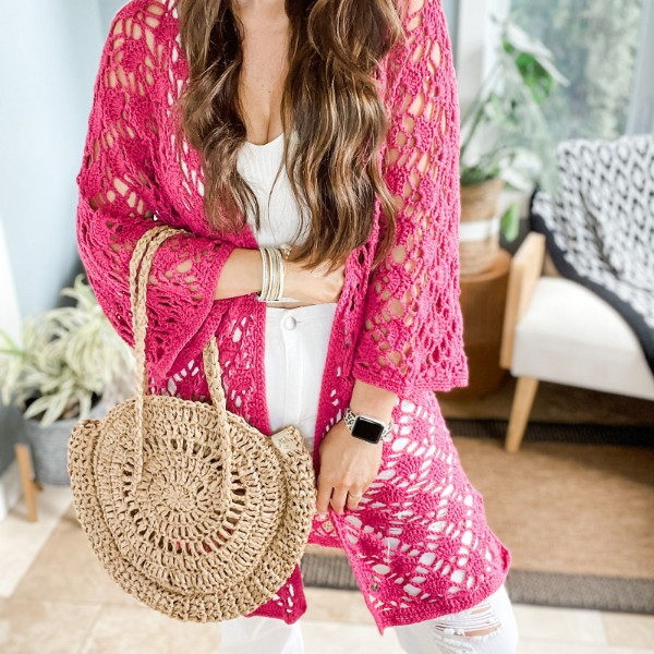 A woman wearing a bright pink, lacy crochet cardigan.