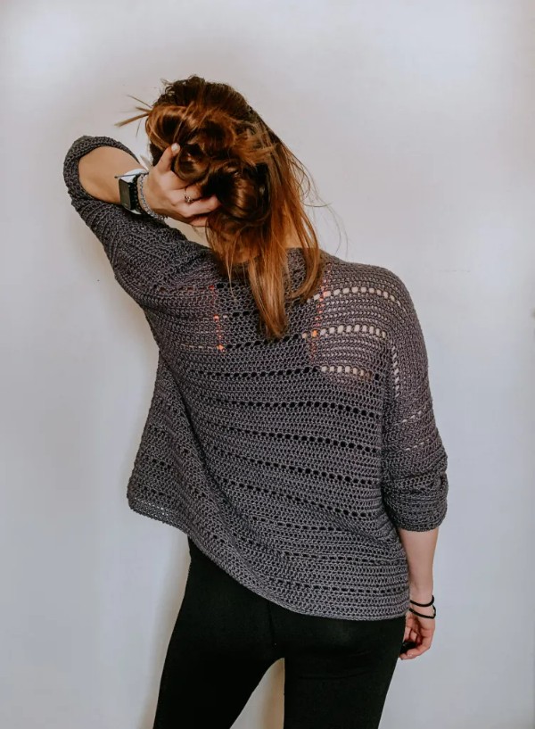 Back view of a woman wearing a charcoal coloured crochet cardigan with an airy stitch pattern.
