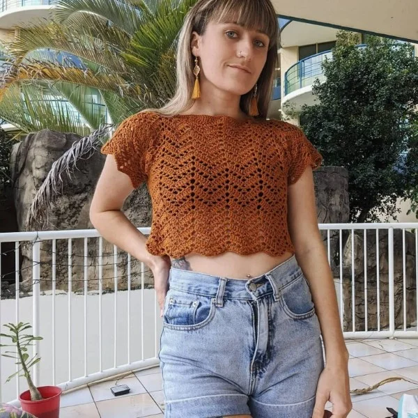 A wman wearing a rust-coloured, cropped crochet lace top.