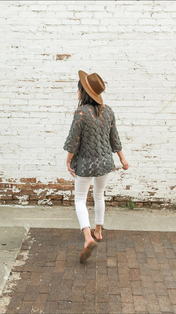 Back view of a woman wearing a khaki coloured lacy crochet cardigan with white jeans.