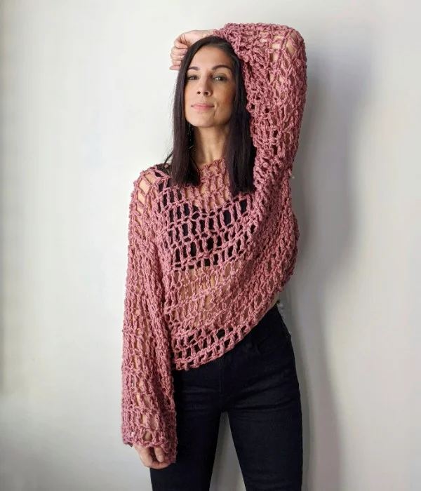 A woman wearing a long sleeved crochet lace sweater top.