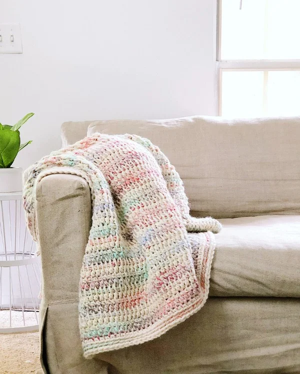 A pastel coloured Tunisian crochet blanket draped over a sofa.