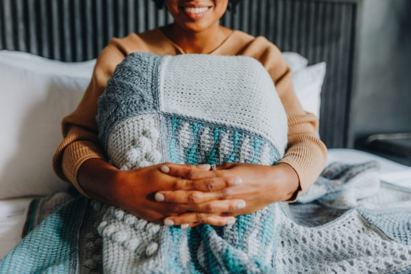 A woman on a bed with a Tunisian cochet sampler blanket on her knees.