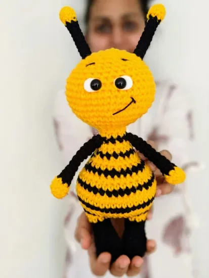 A woman holding a crochet bee toy.
