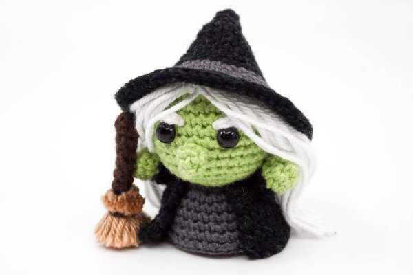 A mini crochet witch with green skin. and a broomstick.