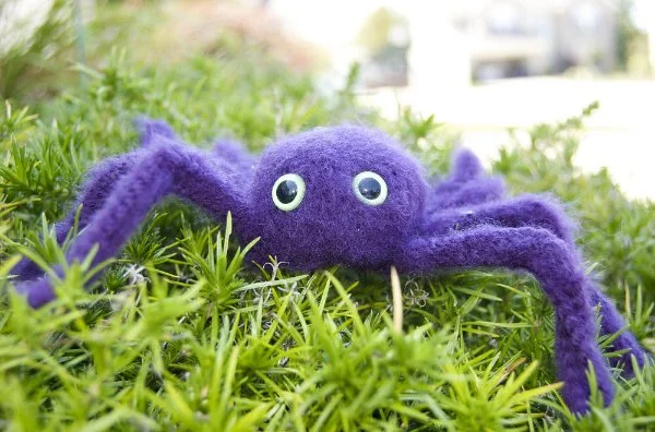 A purple crochet spider on a lawn.
