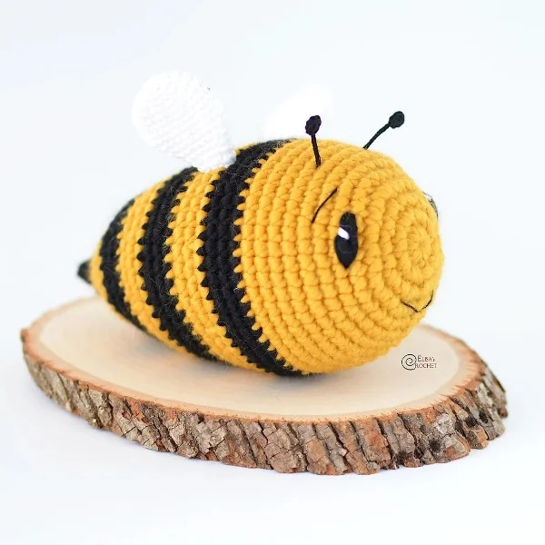 A chubby crochet bee toy sitting on a round of timber.