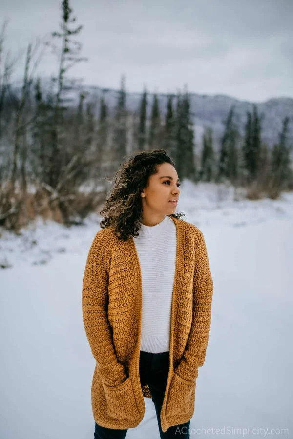 A woman in the snow wearing a cozy long crochet cardigan with pockets.