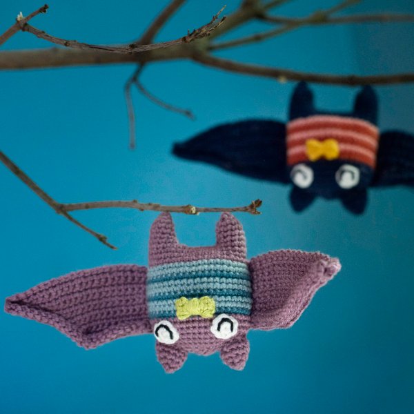 Two crochet bats hanging upside down in a tree.