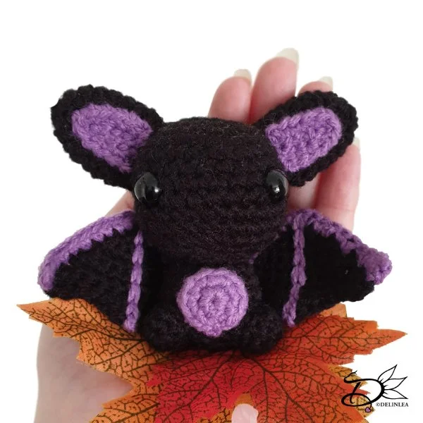A purple and black amigurumi bat sitting on an autumn leaf.