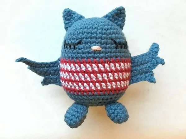 A blue crochet bat amigurumi in a striped sweater.