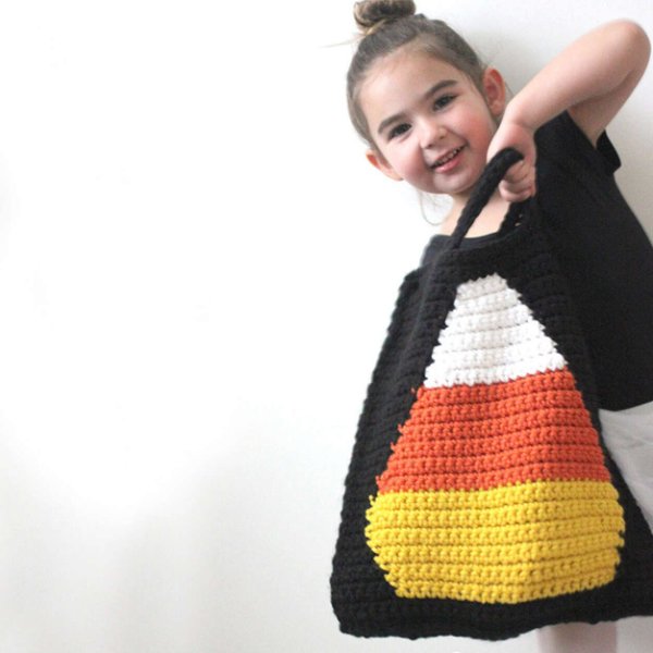 A child holding a crochet Halloween treat bag with a candy corn motif.