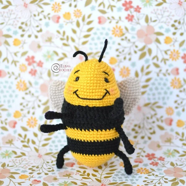 A smiling crochet bee on a floral background.