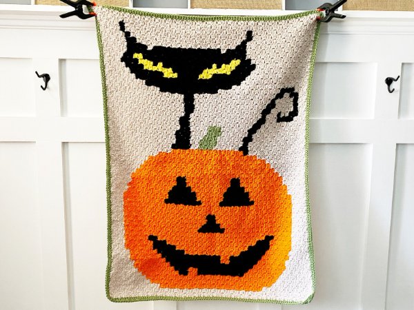 A crochet Halloween blanket with a black cat and a jack-o-lantern.