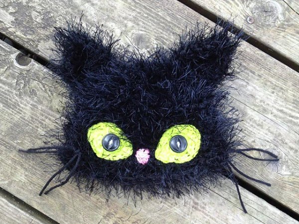 A furry crochet cat hat with bright green eyes.