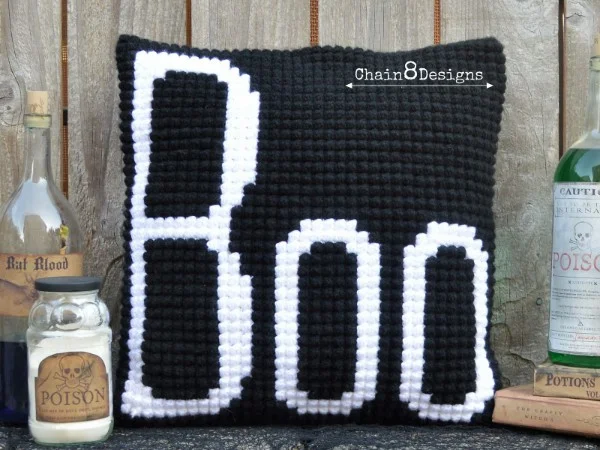 A black crochet pillow with the word boo on it.