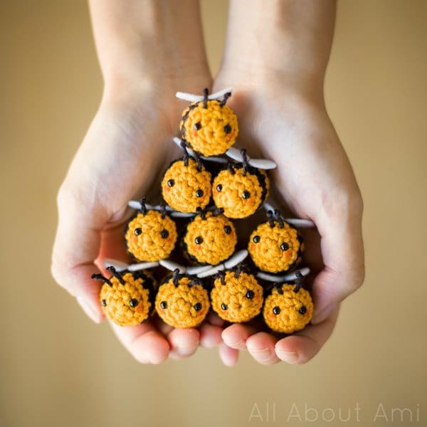 Ten tiny crochet bees stacked in a pyramid held in someones hands.