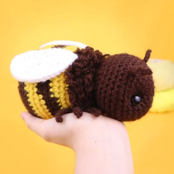 A person holding a chubby crochet bumblebee with a furry thoracic band.