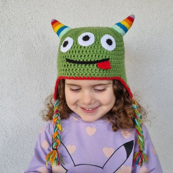 A little girl wearing a crochet monster hat with three eyes.