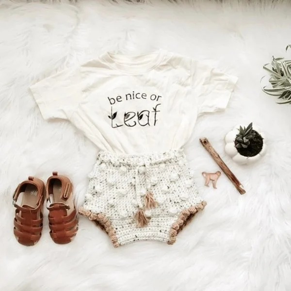 A flat lay image of crochet baby shorts, baby sandals, and a t-shirt.