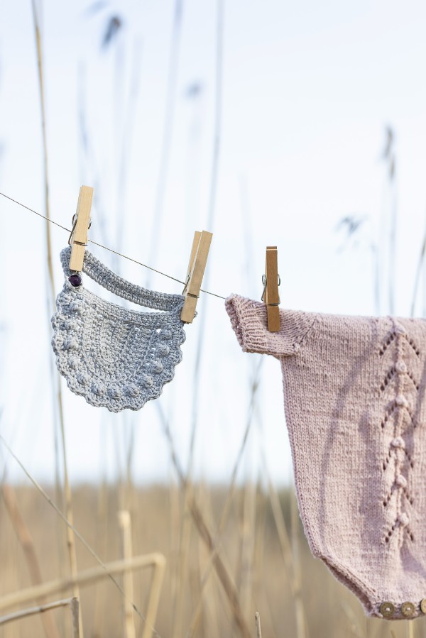A boho-style crochet bib hanging on a clothes line with wooden pegs.
