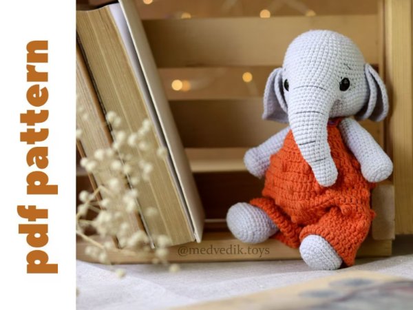 A grey crochet elephant wearing orange crochet overalls.