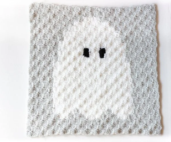 A grey and white crochet blanket with a ghost motif.