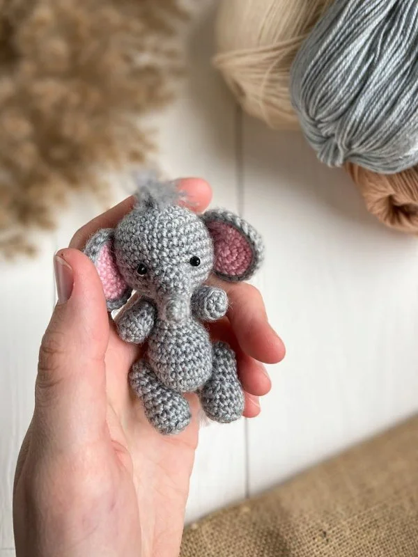 A mini elephant amigurumi resting in the palm of a hand.