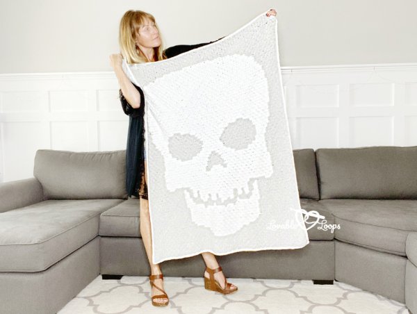 A woman holding up a grey and white crochet skulll blanket.