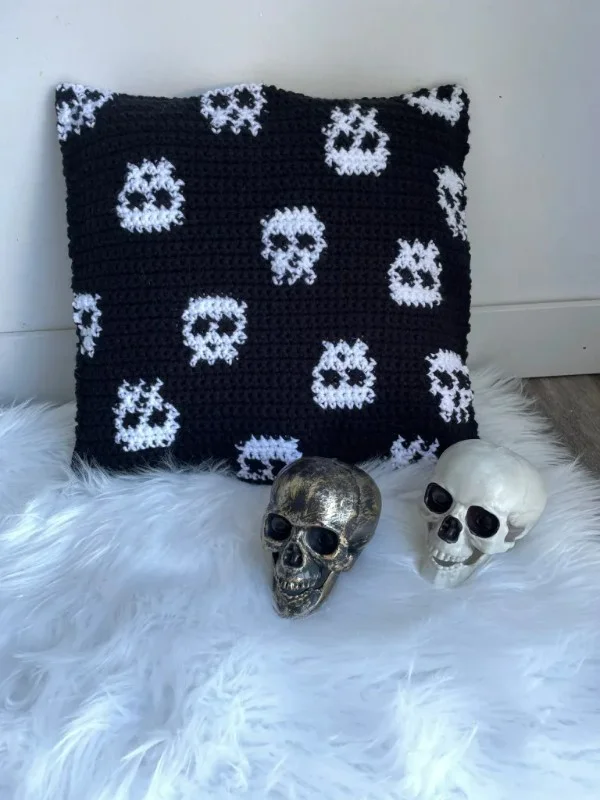 A halloween crochet pillow faeturing mini skulls.
