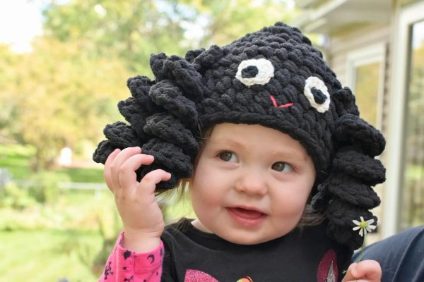 A toddler wearing a black crochet spider hat.