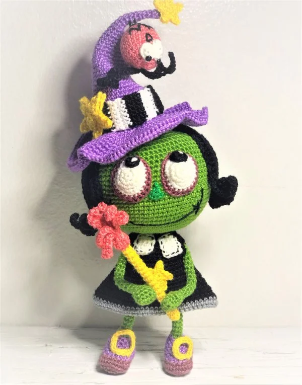 A colourful crochet witch doll with green skin.