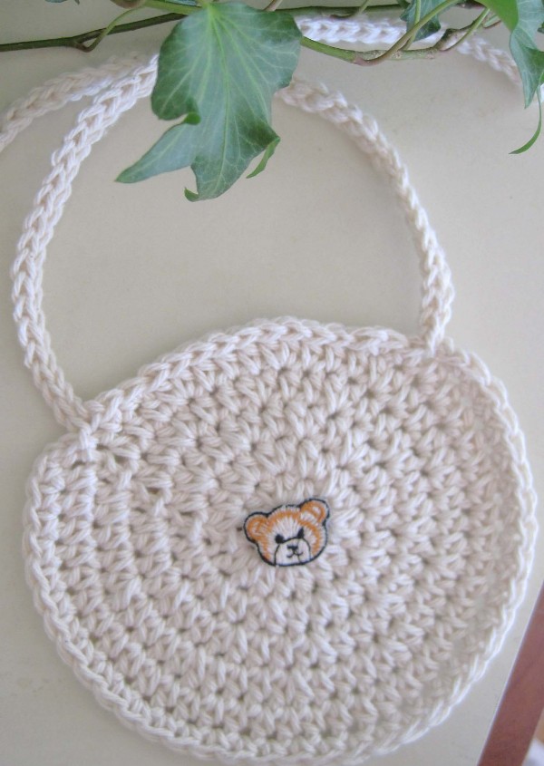 A white crochet bib with a teddy bear applique.