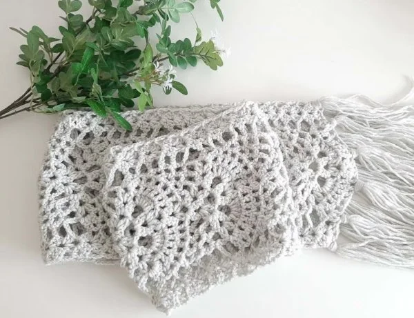 A light grey crochet scarf featuring a lacy fan stitch.