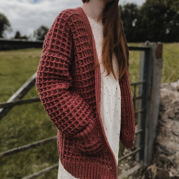 A woman wearing a long,textured crochet cardgian with pockets.