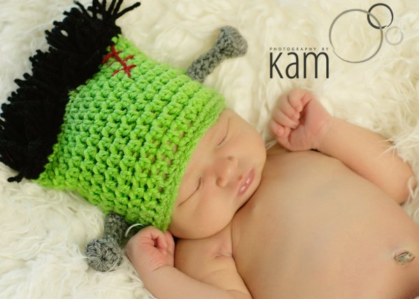 A newborn baby wearing a crochet Frankenstien Halloween hat.