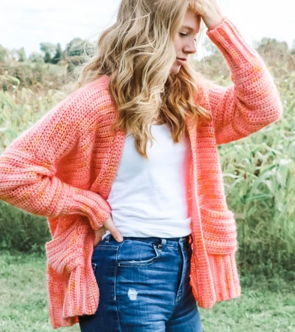 Side view of a woman wearing jeans and a tee with a fuzzy pink cardigan with pockets.