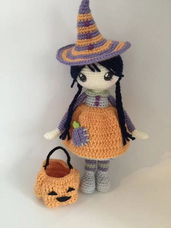 A crochet witch carrying a pumpkin basket made in autumn colours.