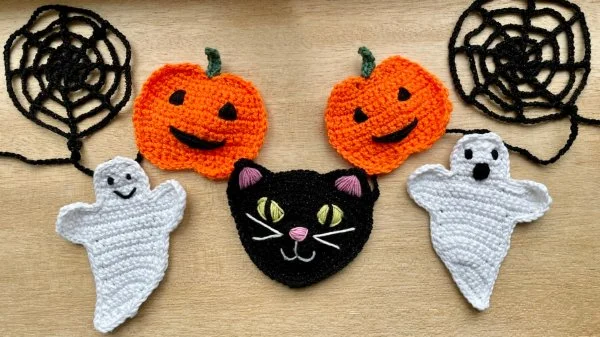 A crochet Halloween garland with pumkin, ghost, and black cat motifs.
