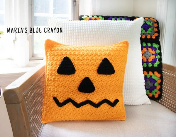 A pumpkin crochet pillow on a couch.
