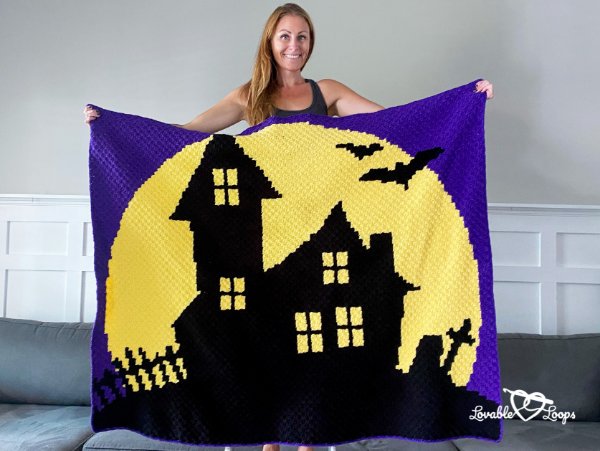 A woman holding a crochet haunted house themed halloween blanket.