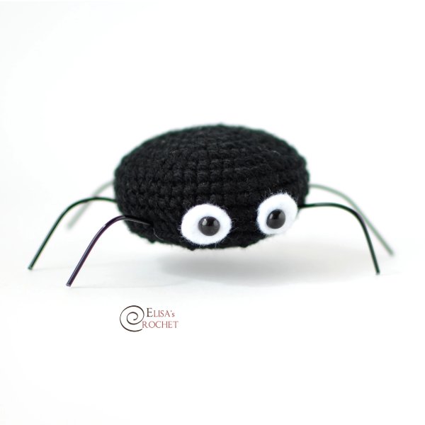 A blac crochet spider with thin legs and bug eyes.